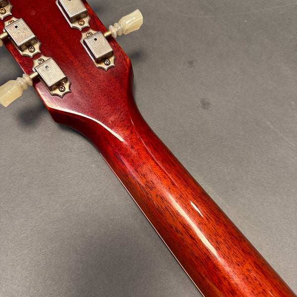 Close-up of glossy mahogany guitar neck and vintage tuning pegs on gray background