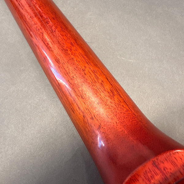 Close-up of polished reddish wooden guitar neck showing wood grain texture against gray background