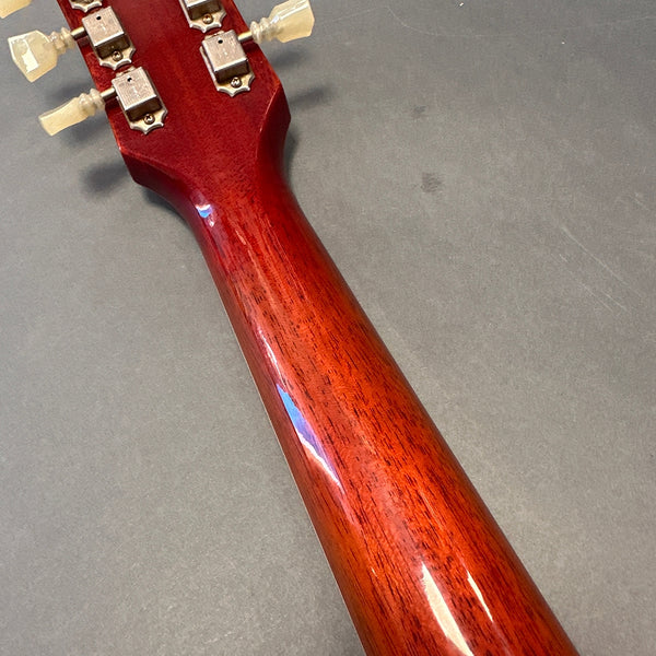 Close-up of the back of a polished mahogany guitar neck with vintage-style tuning pegs on a gray background