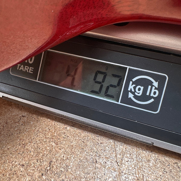 Digital scale showing guitar weight of 4.92 kilograms with red guitar body edge visible on scale at Coffee House Guitars