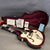 Gretsch hollow body electric guitar in white with Bigsby vibrato, displayed in open black hard case with burgundy plush interior and original paperwork including warranty and guitar guide