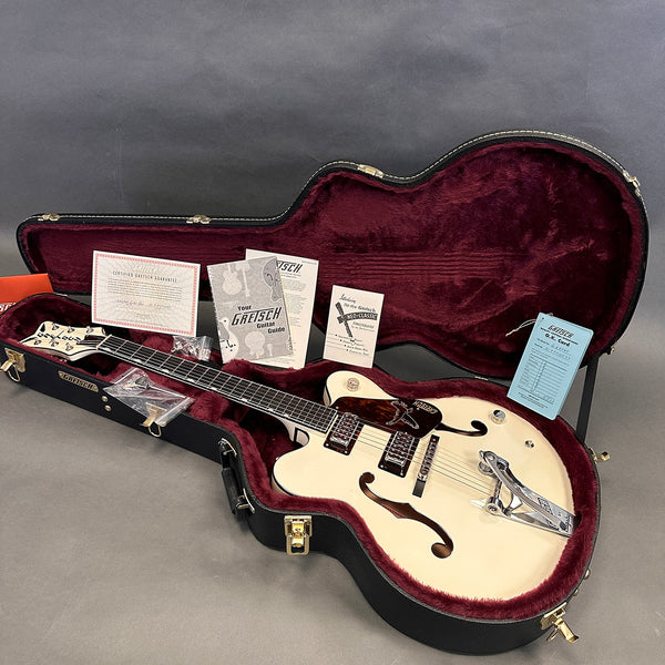 Gretsch hollow body electric guitar in white with Bigsby vibrato, displayed in open black hard case with burgundy plush interior and original paperwork including warranty and guitar guide