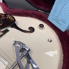 Close-up of white Gretsch hollow body electric guitar with Bigsby tremolo, showing f-hole, control knob, and part of warranty card in plush red case
