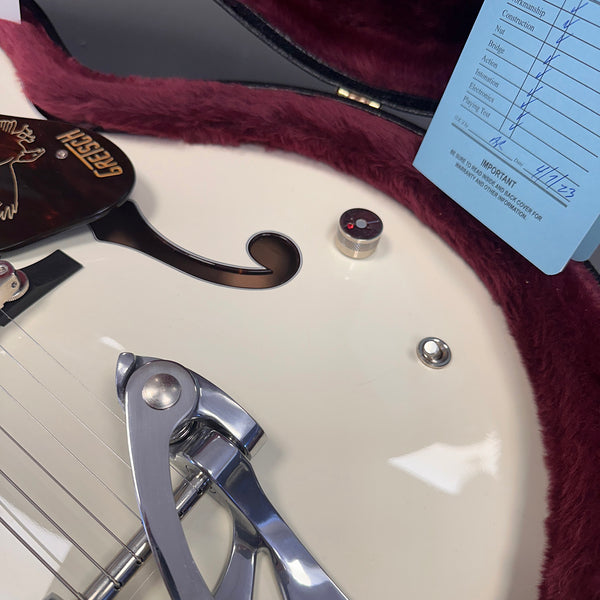 Close-up of white Gretsch hollow body electric guitar with Bigsby tremolo, showing f-hole, control knob, and part of warranty card in plush red case
