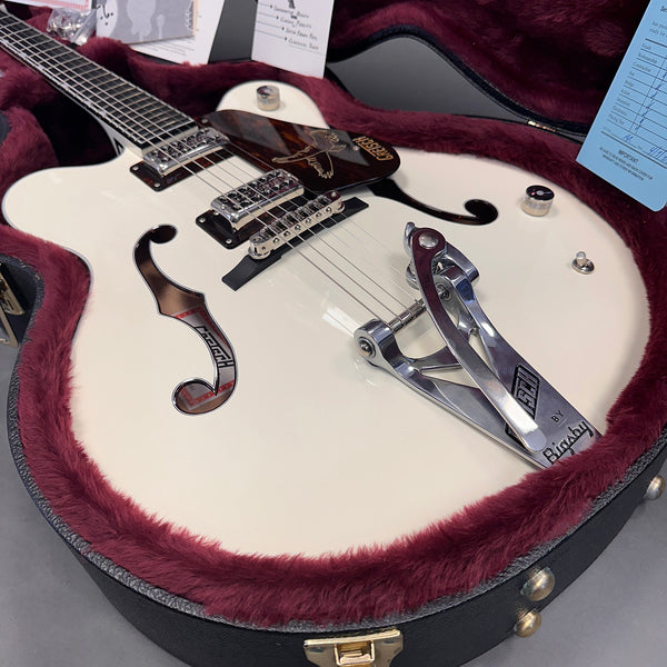 White hollow body electric guitar with Bigsby vibrato tailpiece and chrome hardware in a plush burgundy-lined guitar case