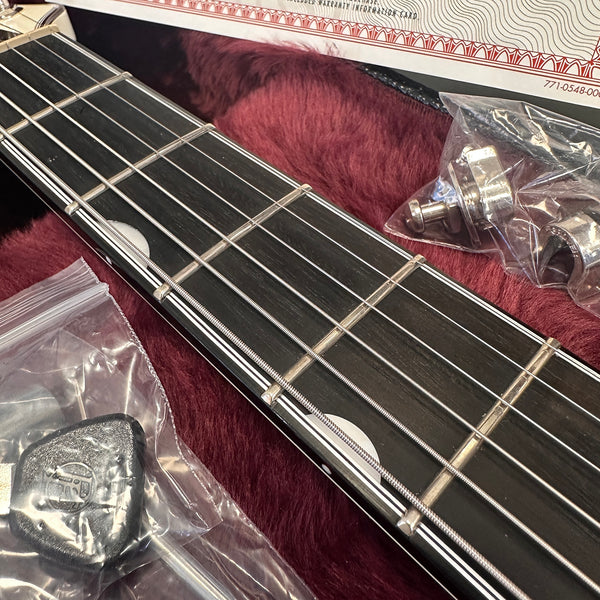 Close-up of acoustic guitar fretboard with steel strings, plastic guitar tool, and metal strap buttons in protective plastic bags on red plush guitar case lining