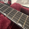 Close-up view of guitar fretboard and strings inside a plush burgundy guitar case with a warranty card visible in the background