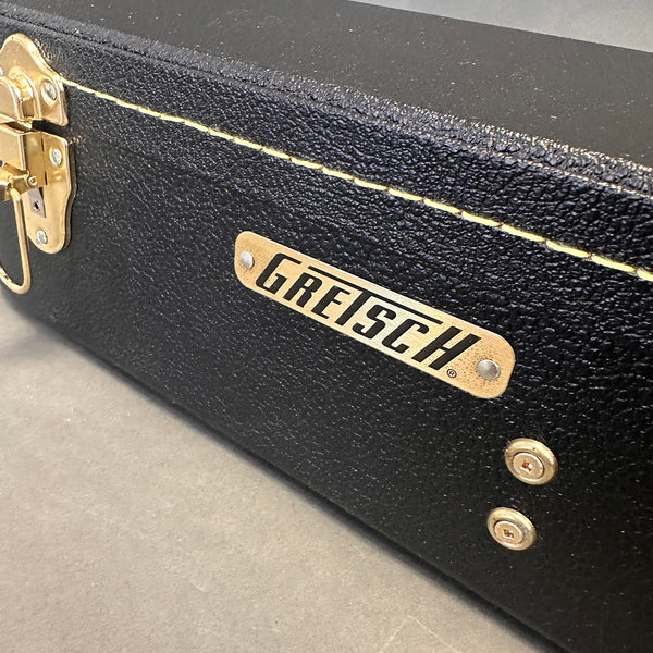 Close-up of black textured Gretsch guitar hard case with gold hardware and logo plaque