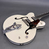 White Gretsch hollow body electric guitar with Bigsby tremolo, dual humbucker pickups, tortoiseshell pickguard with eagle design, and f-holes on gray background