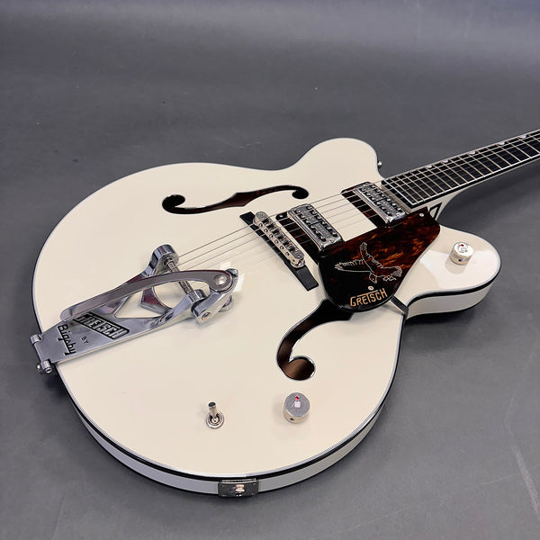 White Gretsch hollow body electric guitar with Bigsby tremolo, dual humbucker pickups, tortoiseshell pickguard with eagle design, and f-holes on gray background