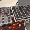 Close-up of electric guitar strings, chrome pickup, tortoiseshell pickguard, and ebony fretboard with white binding and frets.