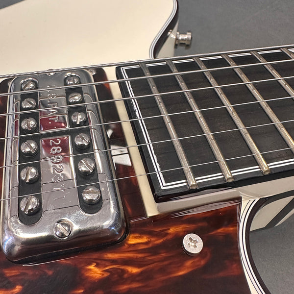 Close-up of electric guitar strings, chrome pickup, tortoiseshell pickguard, and ebony fretboard with white binding and frets.