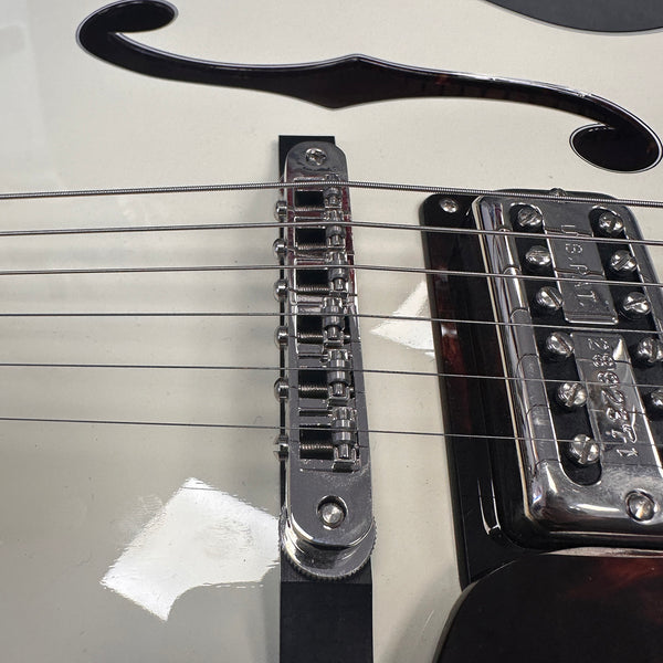 Close-up of white electric guitar bridge and pickup with metal strings and black f-hole detail