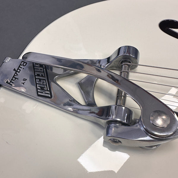 Close-up of chrome Bigsby vibrato tailpiece on white Gretsch electric guitar body with strings attached