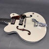 White hollow body electric guitar with Bigsby tremolo, dual humbucker pickups, and tortoiseshell pickguard on gray background