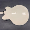 Glossy white semi-hollow electric guitar back with black binding on dark grey surface
