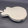 White semi-hollow body electric guitar back with black binding and chrome strap button on gray background