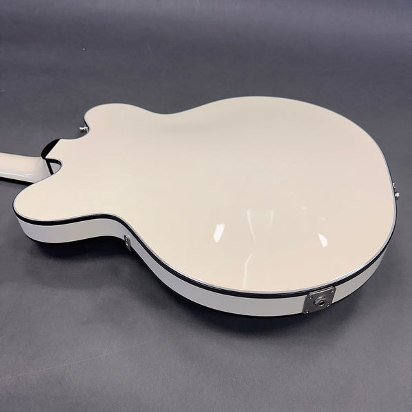 White semi-hollow body electric guitar back with black binding and chrome strap button on gray background