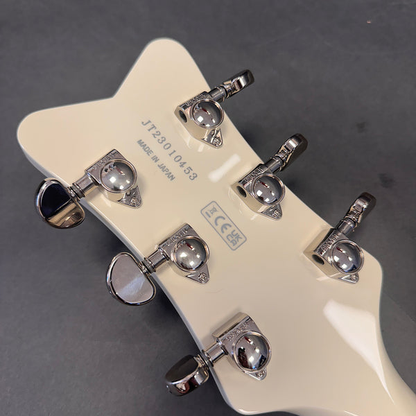 Close-up of white guitar headstock with six chrome tuning pegs, serial number JT23010453, and "Made in Japan" stamp on a dark background
