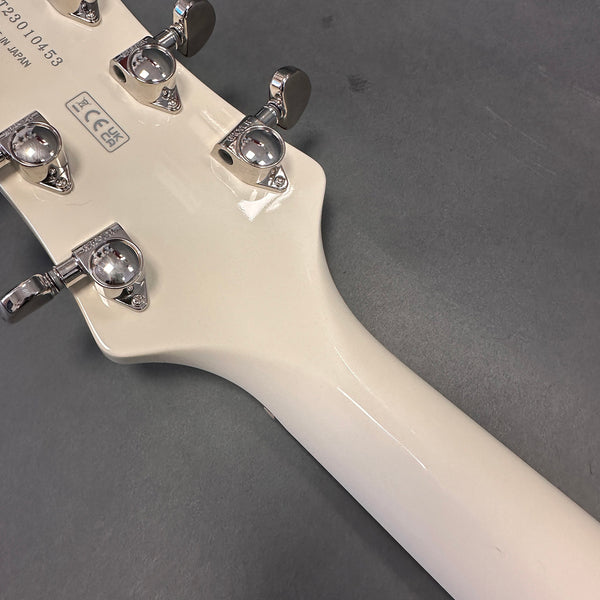 Close-up of the back of a white guitar headstock with chrome tuning pegs and serial number, made in Japan, on a gray surface.