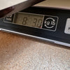 Digital scale displaying the weight of a guitar at 8 pounds 3 ounces on a cork surface, used to measure Coffee House Guitars products.