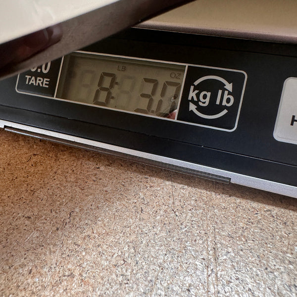 Digital scale displaying the weight of a guitar at 8 pounds 3 ounces on a cork surface, used to measure Coffee House Guitars products.