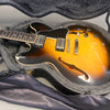 Semi-hollow body electric guitar with sunburst finish and dual humbucker pickups inside a black plush-lined hard case