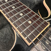 Close-up of electric guitar rosewood fretboard with dot inlays and metal strings on black body