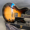 Sunburst semi-hollow electric guitar with dual humbucker pickups, black pickguard, and control knobs, resting in an open black hard case with plush interior lining.