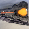 Electric semi-hollow body guitar with sunburst finish lying face down in open black hard case with gray plush interior and soft cover on gray surface