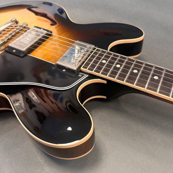 Close-up of semi-hollow body electric guitar with sunburst finish, dual humbucker pickups, and rosewood fretboard on gray background