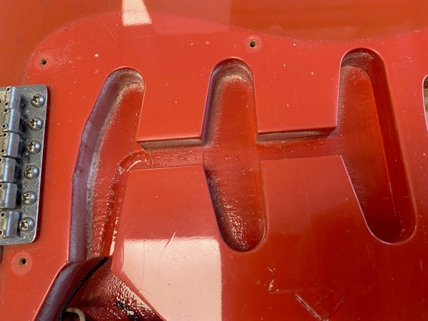 Close-up of red electric guitar body routing cavities for pickups and bridge hardware without pickups installed