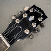 Close-up of black Gibson guitar headstock with silver tuning pegs and logo on gray background