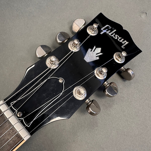 Close-up of black Gibson guitar headstock with silver tuning pegs and logo on gray background