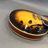 Close-up view of sunburst semi-hollow electric guitar body showing control knobs, pickup selector switch, and bridge on gray background