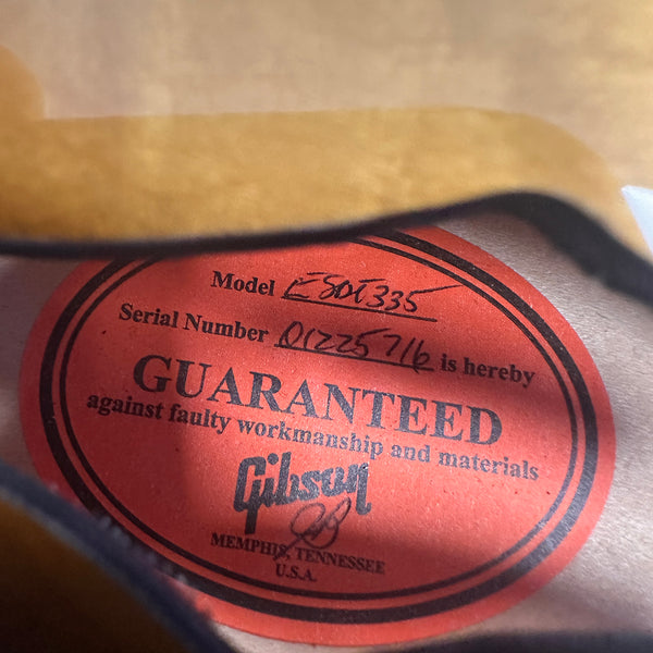 Close-up of a red Gibson guitar label inside a guitar body showing model E 80 1335 and serial number 01225716, guaranteed against faulty workmanship and materials, made in Memphis, Tennessee, USA.