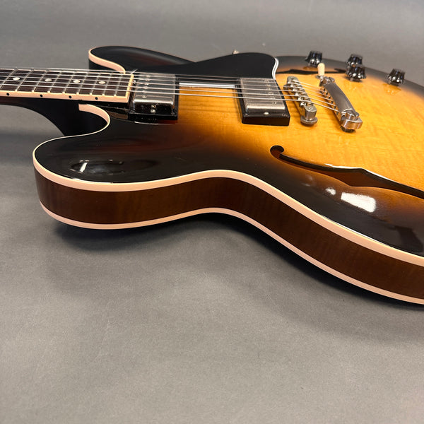 Close-up of semi-hollow body electric guitar with sunburst finish, dual humbucker pickups, and cream binding on a grey background