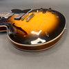 Close-up of sunburst semi-hollow body electric guitar with F-hole and control knobs on gray background