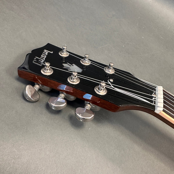 Close-up of Gibson acoustic guitar headstock with tuning pegs and strings on gray background