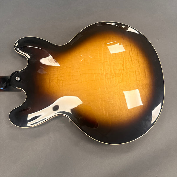 Back side of a semi-hollow electric guitar with sunburst finish and cream binding on gray background