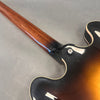 Close-up of a semi-hollow body electric guitar neck joint with sunburst finish and strap button on a gray background