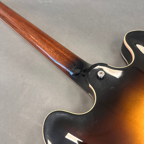 Close-up of a semi-hollow body electric guitar neck joint with sunburst finish and strap button on a gray background