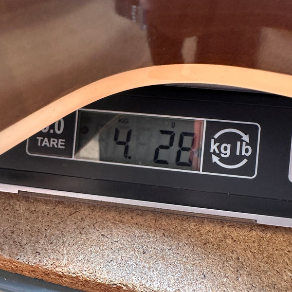 Close-up of digital scale displaying guitar weight of 4.28 kilograms with part of guitar body visible above the scale