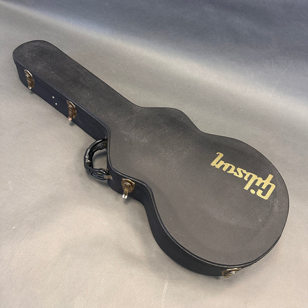 Black Gibson guitar hardshell case with gold logo and metal latches on gray surface