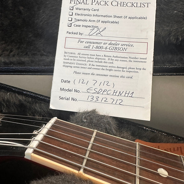 Gibson guitar final pack checklist with warranty card and model number ESDPCHNH1 and serial number 13312712 on top of guitar case lining and guitar neck with strings