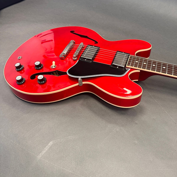 Semi-hollow electric guitar with bright red finish, black pickguard, dual humbucker pickups, four control knobs, and f-holes on gray background