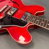 Close-up of red semi-hollow electric guitar body with black pickguard, dual humbucker pickups, and rosewood fretboard on gray background