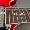 Close-up image of electric guitar fretboard with mother-of-pearl fret markers, metal frets, and six steel strings on a red guitar body