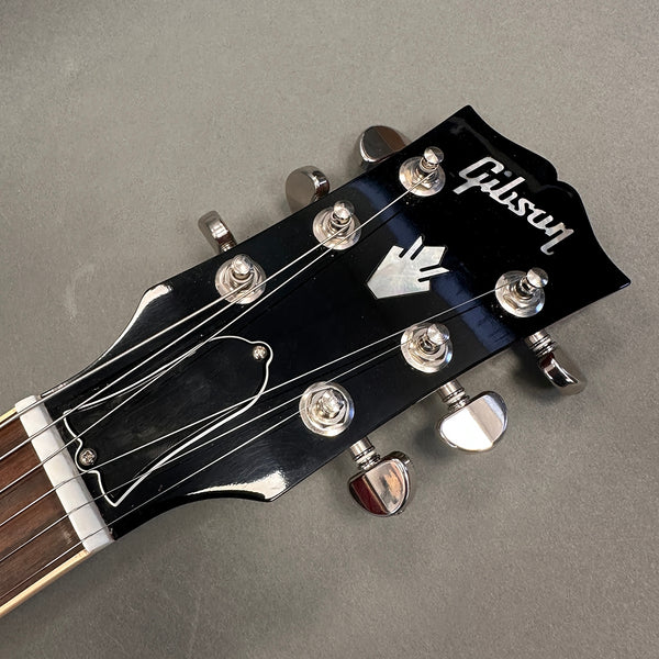 Close-up of black Gibson guitar headstock with six tuning pegs and silver Gibson logo on a gray background
