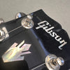 Close-up of black Gibson guitar headstock with mother-of-pearl inlay and tuning pegs